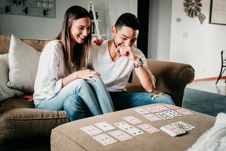 Foto um jovem casal sentado no sofá em casa a jogar cartas.