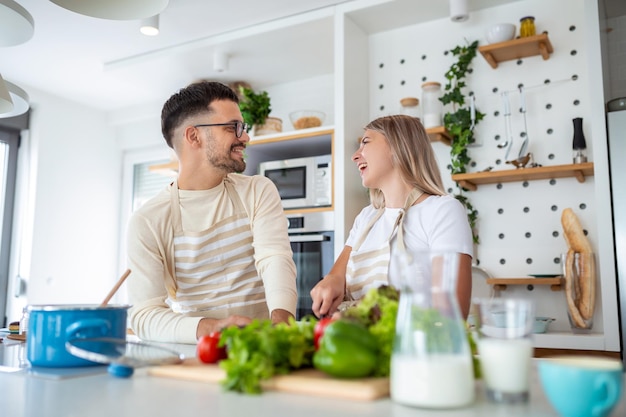 Um jovem casal sorridente a cozinhar comida na cozinha juntos na cozinha a divertir-se juntos homem e mulher a rir