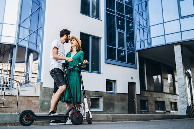 Um jovem casal sorridente desfruta de um passeio na cidade em scooters elétricos.