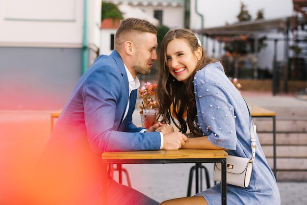 Foto um jovem casal sorridente e feliz se reúne em um encontro, desfruta da vida, sentado em uma mesa de mãos dadas.