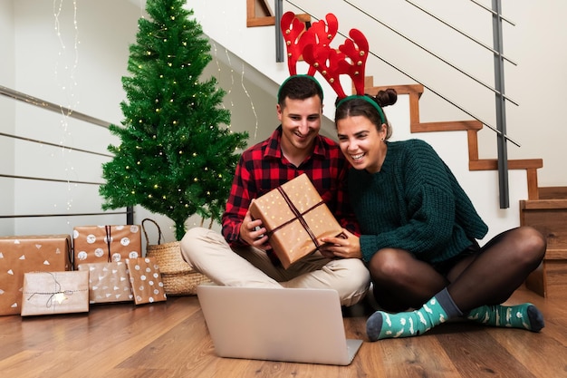 Um jovem casal usando chifres de renas em uma chamada de vídeo mostrando alguns presentes de Natal para a família