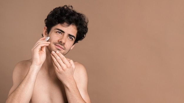 Um jovem caucasiano com barba por fazer está fazendo uma massagem facial usando um gua sha