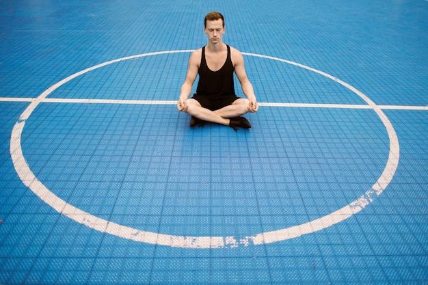 Um jovem caucasiano em roupas esportivas pretas fazendo ioga na academia ao ar livre