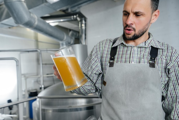 Foto um jovem cervejeiro barbudo conduz o controle de qualidade da cerveja acabada de fazer na cervejaria.