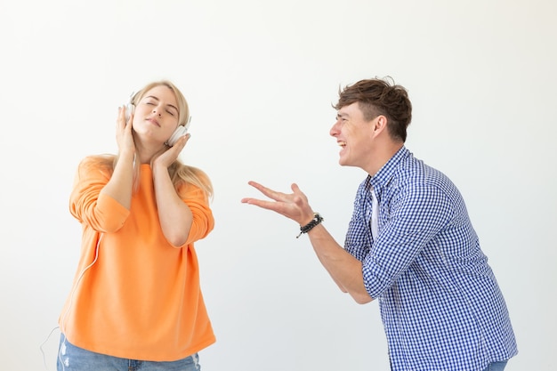 Foto um jovem chateado implora para sua mulher ouvi-lo, mas ela ouve música com fones de ouvido posando em um