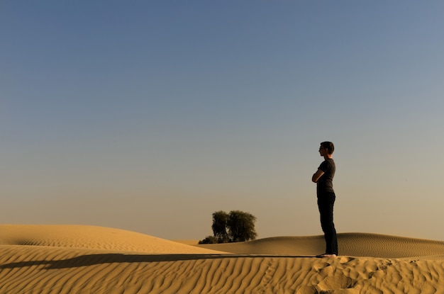 Um jovem chocando em um deserto com as luzes do pôr do sol com sombra longa