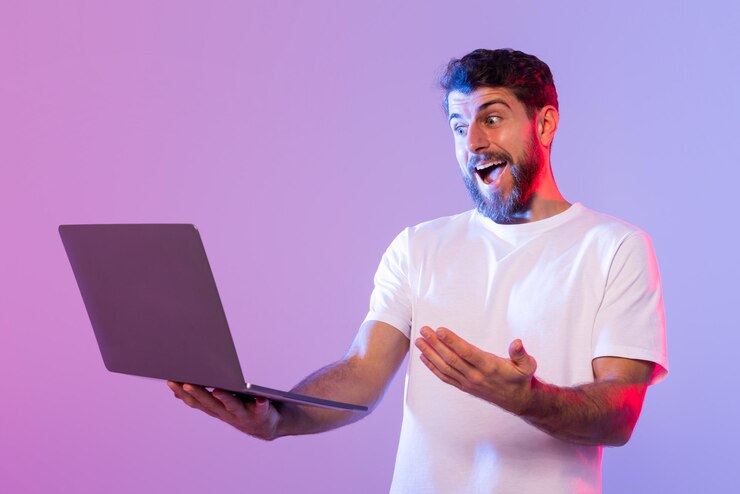 Foto um jovem com barba e vestindo uma camiseta branca está segurando um laptop com um entusiasmo e