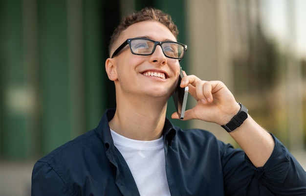 Um jovem com óculos sorrindo enquanto fala em um smartphone