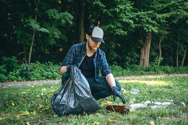 Um jovem com um saco de lixo na floresta limpa garrafas plásticas