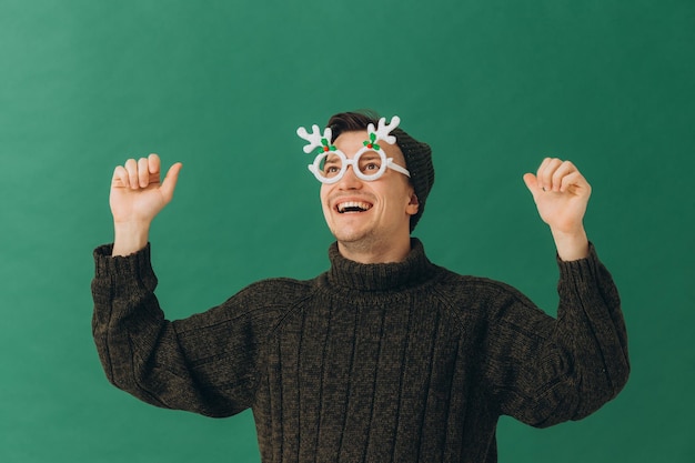 Um jovem com um suéter quente, um boné e óculos de carnaval isolados em um fundo verde