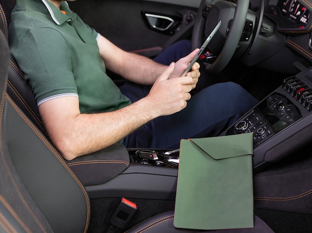Foto um jovem com um tablet na mão para o carro esporte. multitarefa