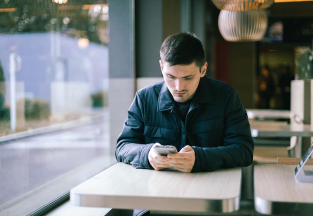 Um jovem com um telefone nas mãos está sentado em uma lanchonete