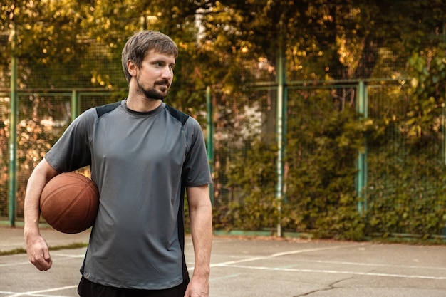 Um jovem com uma bola de basquete na mão em uma quadra de esportes aberta Conceito esportivo