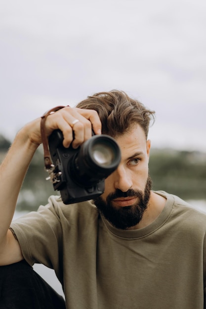 Um jovem com uma câmera SLR moderna em suas mãos em um fundo natural