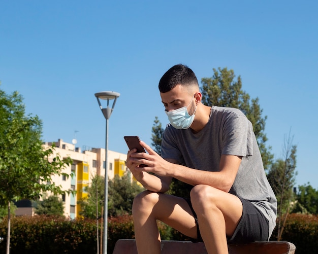 Um jovem com uma máscara médica no parque fala no telefone celular