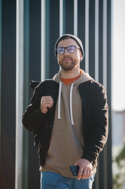 Um jovem com uma mochila e roupas casuais no fundo de um prédio de escritórios