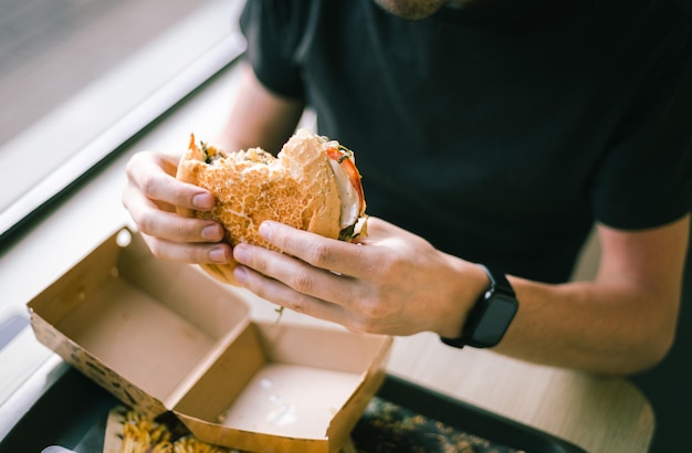 Um jovem come fast-food em uma lanchonete