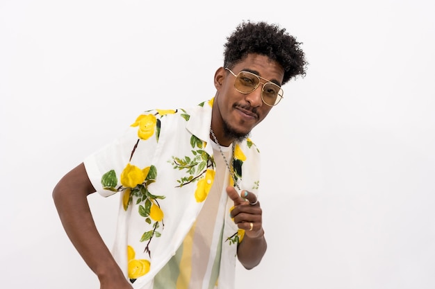 Um jovem cubano com uma camisa de flores branca e verde, óculos, sorrindo e dançando sobre um fundo branco, copie o espaço e cole