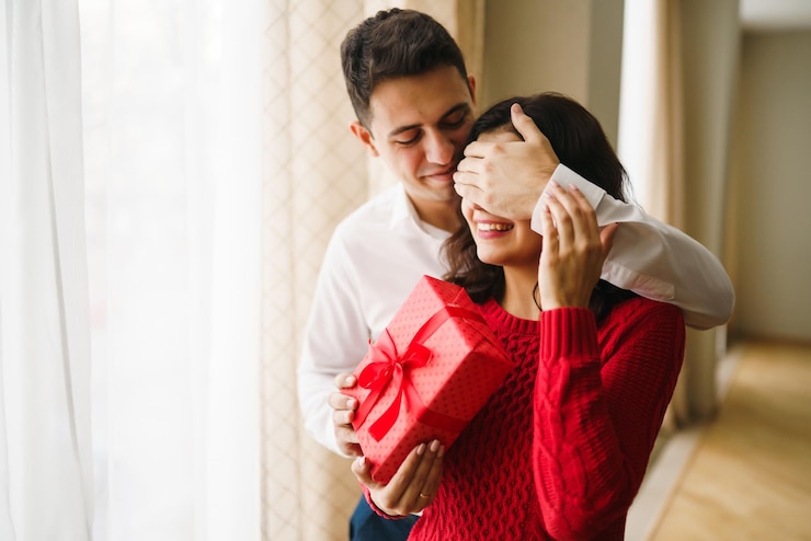 Foto um jovem dá um presente à sua amada e fecha os olhos com a mão