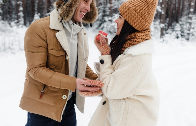 Um jovem dá um presente para uma garota em uma floresta coberta de neve. Surpresa para o Dia dos Namorados.