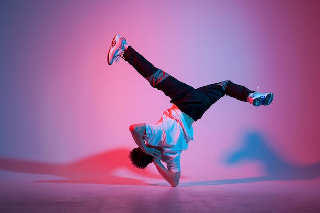 Um jovem dançarino está dançando em uma iluminação de néon. Um acrobata está fazendo um truque.