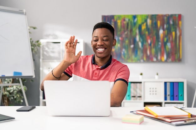 Um jovem de beleza afro-americana senta-se à mesa em uma sala de escritório com um laptop