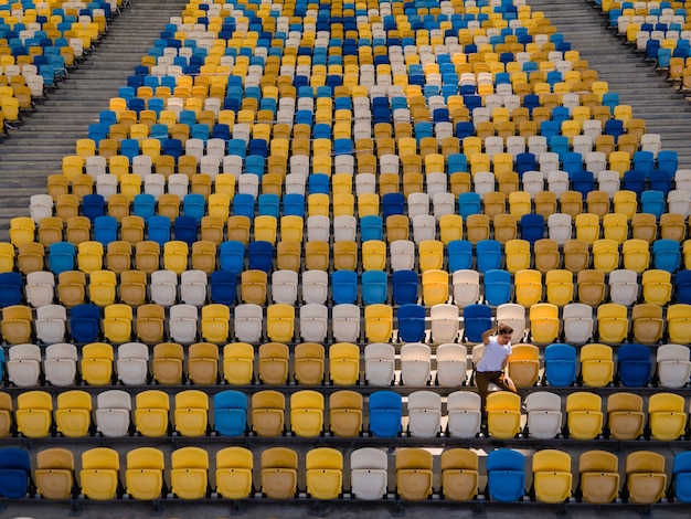 Um jovem de camiseta branca cantando em uma tribuna vazia de um estádio de futebol