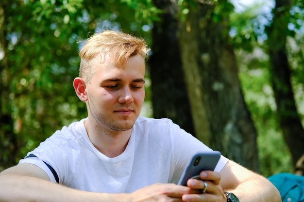 Um jovem de camiseta branca se comunica via SMS com um amigo Emoções alegres da comunicação