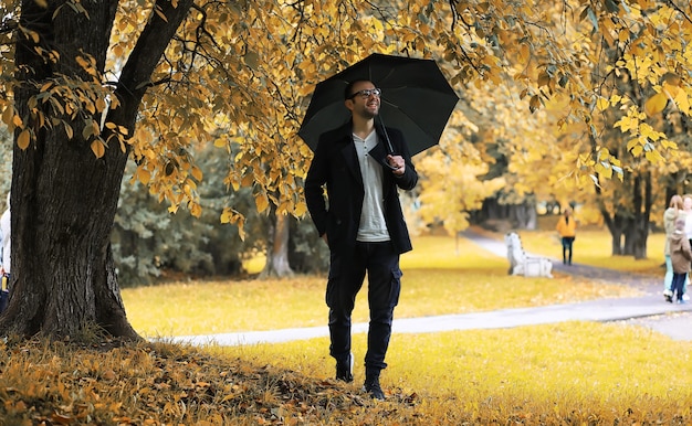 Um jovem de óculos anda no parque com um guarda-chuva durante a chuva.