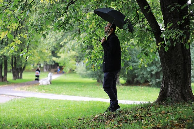 Um jovem de óculos anda no parque com um guarda-chuva durante a chuva.