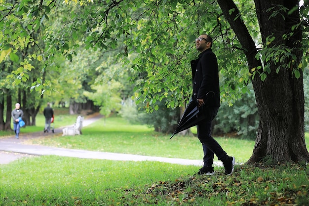 Um jovem de óculos anda no parque com um guarda-chuva durante a chuva.