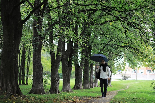 Um jovem de óculos caminha no parque com um guarda-chuva durante a chuva