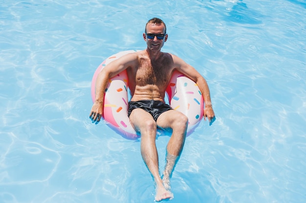 Foto um jovem de óculos escuros e shorts está relaxando em uma rosquinha inflável nas férias de verão da piscina