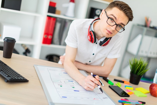 Um jovem de óculos fica perto de um computador desk.ng.