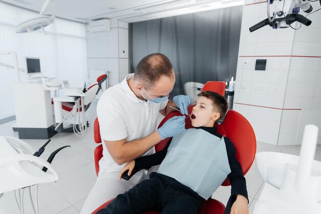 Um jovem dentista examina e trata os dentes de um menino de oito anos na odontologia branca moderna closeup Tratamento de próteses dentárias e clareamento dos dentes Prevenção da odontologia moderna