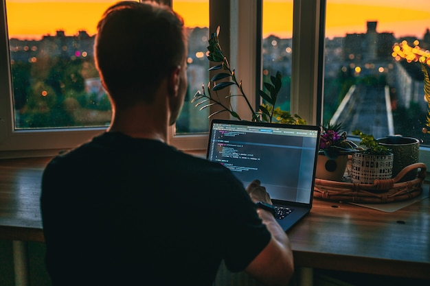 Um jovem desenvolvedor está programando um script de código tarde da noite com belas luzes da cidade