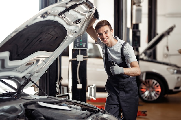 Um jovem e atraente mecânico de automóveis está sorrindo: serviço e manutenção de automóveis.