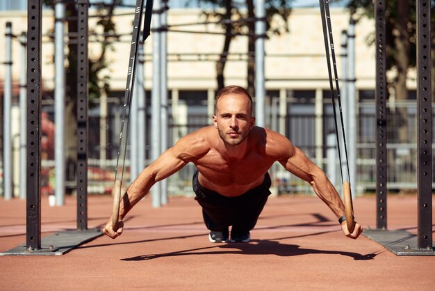 Foto um jovem e bonito homem está fazendo algumas flexões ele está usando loops para isso