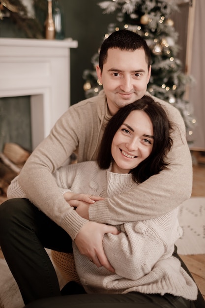 Um jovem e uma jovem se amando se abraçando em suéteres aconchegantes perto de uma árvore de Natal em casa