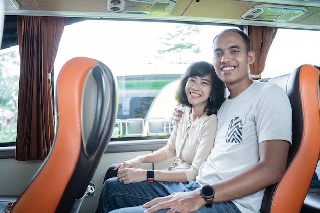 Um jovem e uma jovem sorriem enquanto se sentam lado a lado em um assento de ônibus enquanto viajam