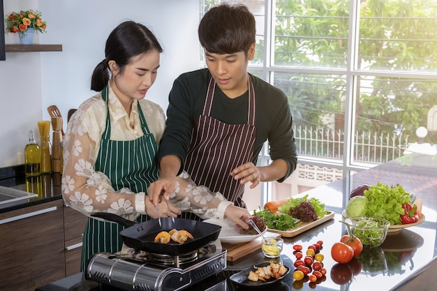 Um jovem e uma linda adolescente asiática estão felizes em fazer salada de camarão em uma cozinha moderna.