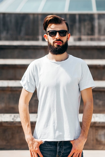 Um jovem elegante com barba, uma camiseta branca e óculos