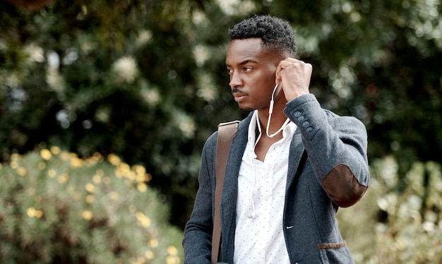 Um jovem elegante e sério que vai trabalhar enquanto ouve música usando fones de ouvido Um jovem empresário afro-americano andando ao ar livre com bom estilo ou moda