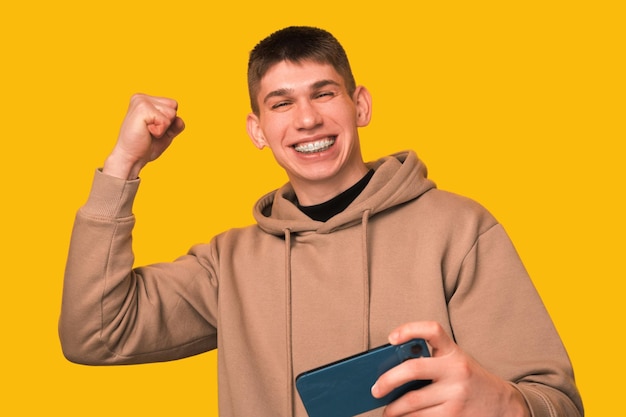 Um jovem em êxtase está tocando ao telefone e mostrando o gesto vencedor