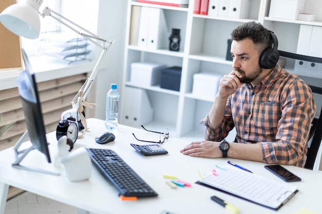 Um jovem em fones de ouvido se senta em uma mesa no escritório e olha para o monitor.