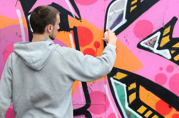 Um jovem em um capuz cinza pinta graffiti em rosa e verde