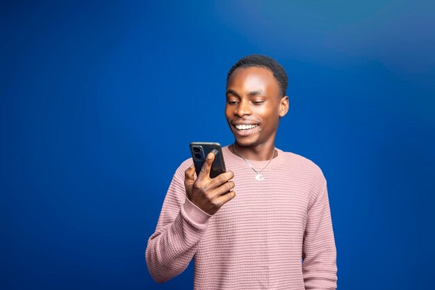 Um jovem empreendedor adulto nigeriano segura um smartphone felizmente navegando e usando tecnologia sem fio para comunicação e mídias sociais em uma tomada de estúdio positiva