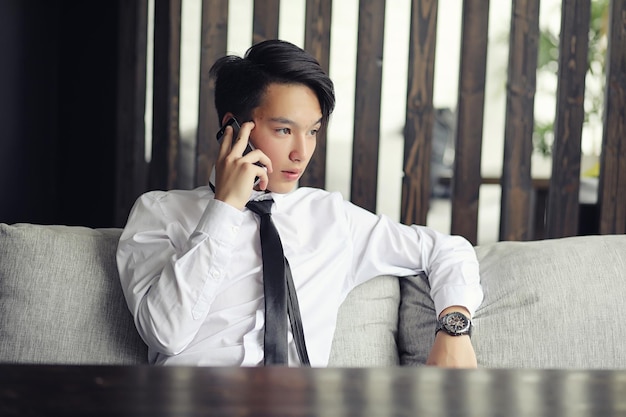 Um jovem empresário asiático está esperando por um parceiro em um café. Reunião de negócios no restaurante. Um jovem coreano falando ao telefone em um café.