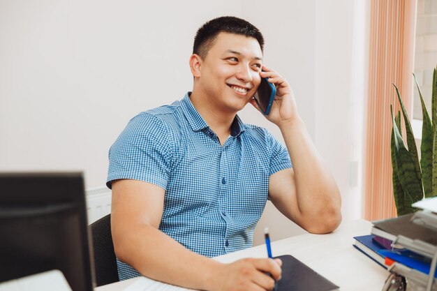 Um jovem empresário asiático está falando ao telefone para discutir o trabalho no escritório, o homem é asiático