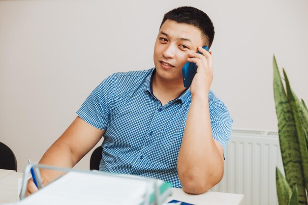 Um jovem empresário asiático está falando ao telefone para discutir o trabalho no escritório, o homem é asiático